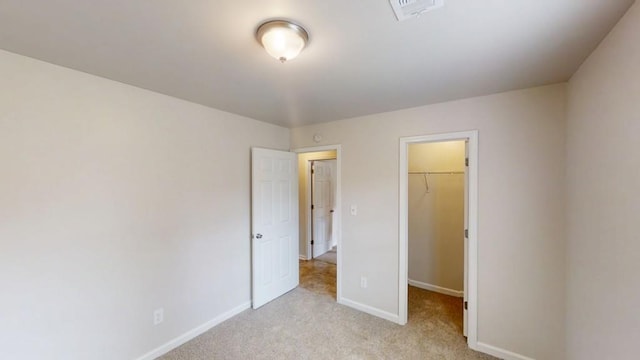 unfurnished bedroom featuring a walk in closet, light colored carpet, baseboards, and a closet