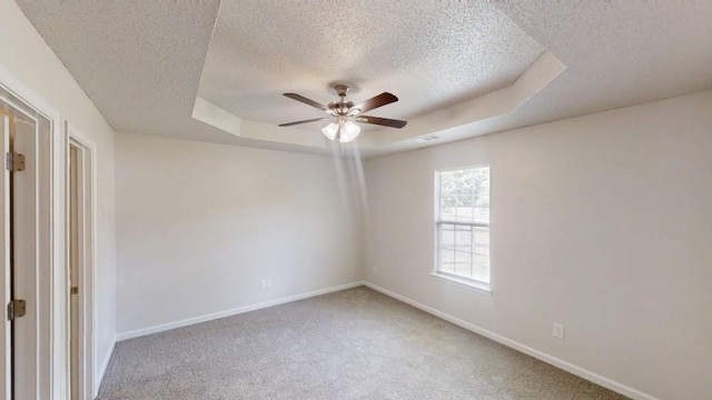 unfurnished room featuring a textured ceiling, a tray ceiling, carpet, ceiling fan, and baseboards