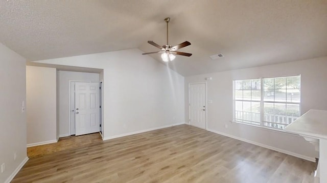 interior space with a ceiling fan, light wood-style flooring, lofted ceiling, a textured ceiling, and baseboards