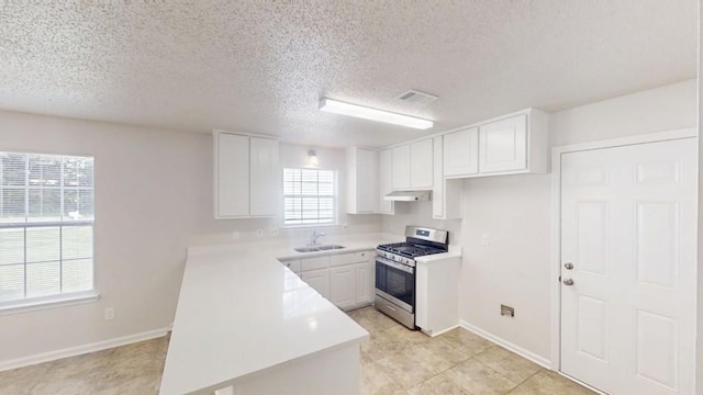 kitchen with stainless steel range with gas stovetop, a sink, a peninsula, light countertops, and baseboards