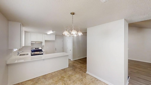 kitchen featuring gas stove, under cabinet range hood, a sink, light countertops, and a chandelier