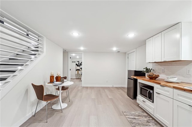 kitchen with white cabinetry, backsplash, butcher block counters, and light wood-type flooring