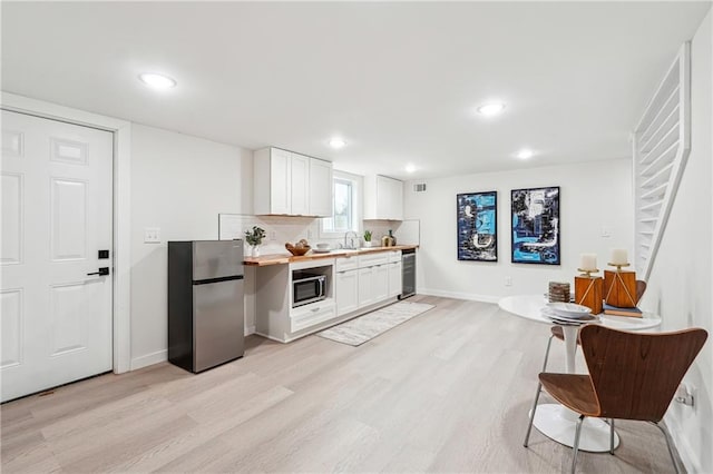 kitchen featuring butcher block countertops, appliances with stainless steel finishes, light hardwood / wood-style floors, white cabinets, and decorative backsplash