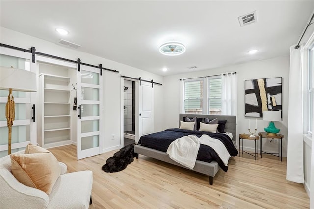 bedroom featuring a spacious closet, a barn door, and light wood-type flooring