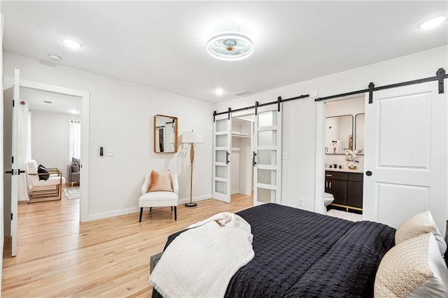 bedroom featuring ensuite bathroom, a barn door, and light hardwood / wood-style floors