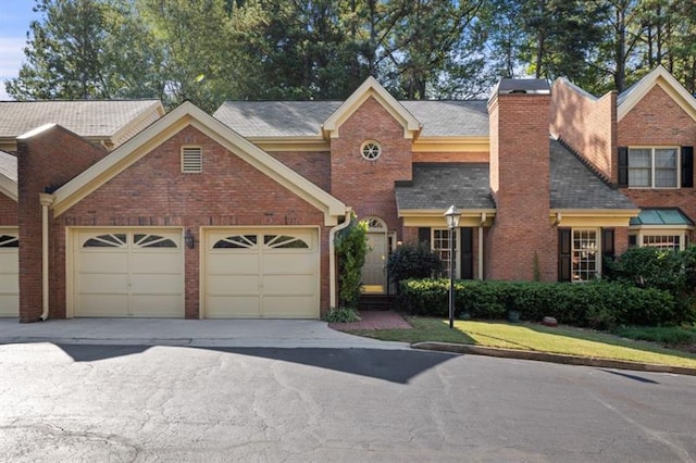 view of front of property featuring a garage, driveway, a chimney, and brick siding