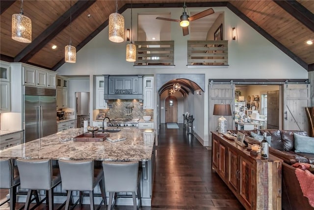 kitchen with a barn door, high vaulted ceiling, decorative light fixtures, and stainless steel built in refrigerator