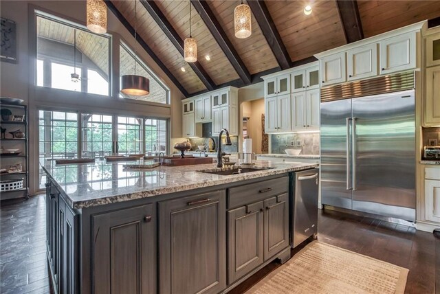 kitchen featuring white cabinetry, decorative light fixtures, appliances with stainless steel finishes, high vaulted ceiling, and a center island with sink