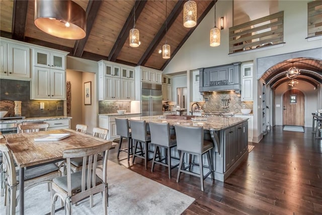 kitchen featuring an island with sink, built in refrigerator, and hanging light fixtures