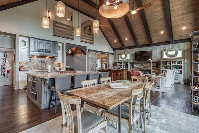 dining room featuring wooden ceiling, dark hardwood / wood-style floors, beam ceiling, and a stone fireplace