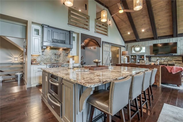 kitchen with wood ceiling, a barn door, a center island with sink, beam ceiling, and a kitchen breakfast bar