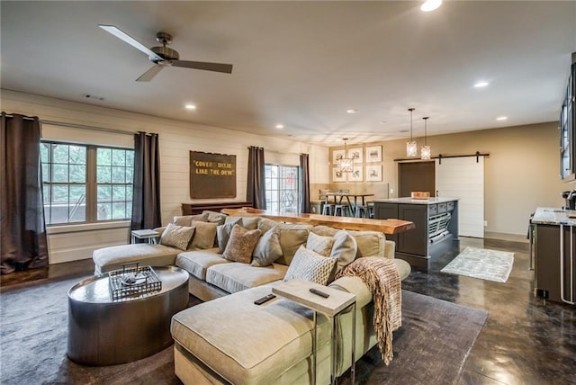 living room with a barn door and ceiling fan with notable chandelier