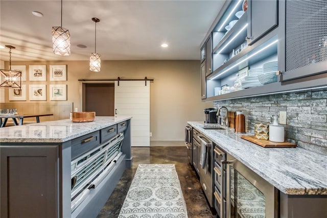 kitchen with a barn door, a center island, light stone counters, and sink