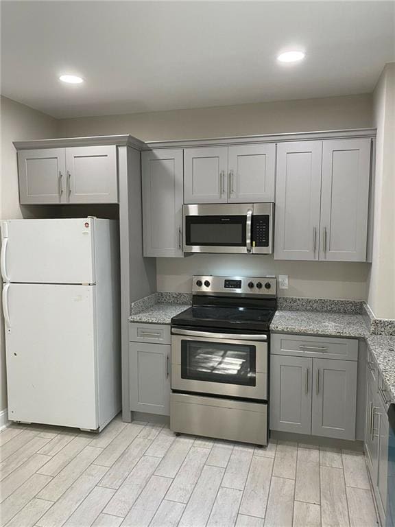 kitchen with appliances with stainless steel finishes, gray cabinetry, light stone countertops, and light hardwood / wood-style floors