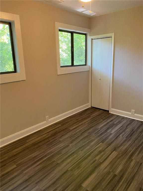 unfurnished bedroom with multiple windows, a closet, and dark hardwood / wood-style flooring