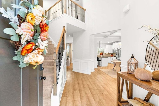 entrance foyer featuring a wainscoted wall, light wood-style flooring, stairway, a high ceiling, and a decorative wall