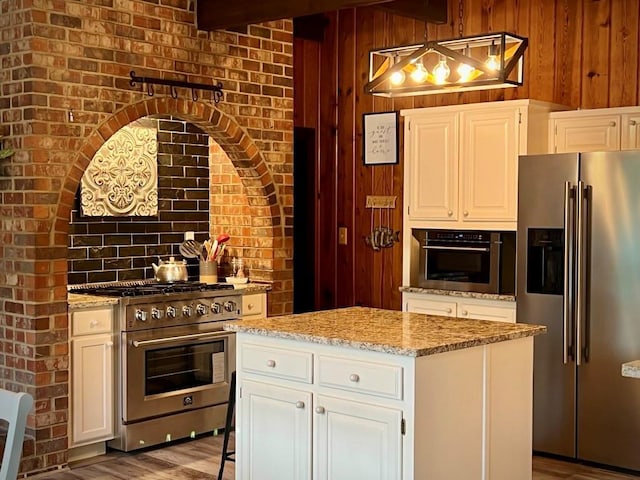 kitchen with hanging light fixtures, premium appliances, brick wall, a center island, and white cabinets