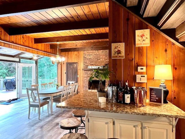 kitchen featuring wood walls, a notable chandelier, light stone counters, beam ceiling, and white cabinetry