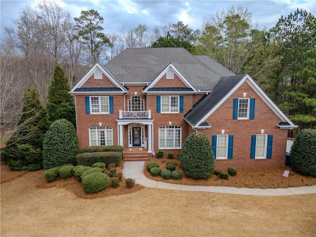 colonial-style house with brick siding, a balcony, and roof with shingles