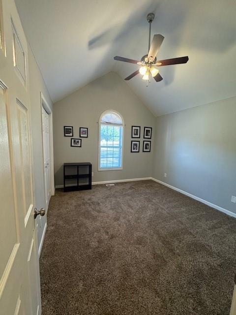 interior space featuring lofted ceiling, dark carpet, and ceiling fan