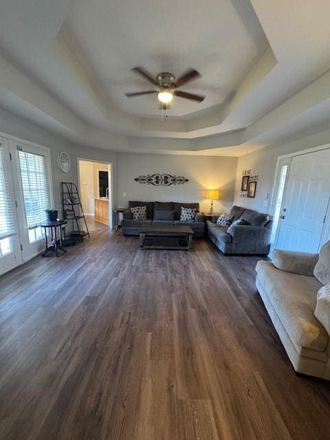 living room with a raised ceiling, dark wood-type flooring, and ceiling fan