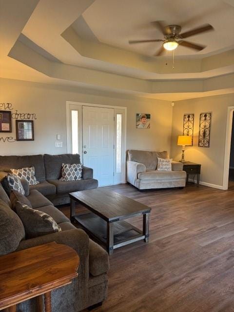 living room featuring a raised ceiling, dark wood-type flooring, and ceiling fan