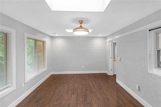 unfurnished room with dark hardwood / wood-style flooring, a skylight, and brick wall