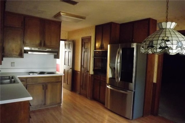 kitchen with sink, light hardwood / wood-style flooring, stainless steel refrigerator with ice dispenser, white cooktop, and black oven