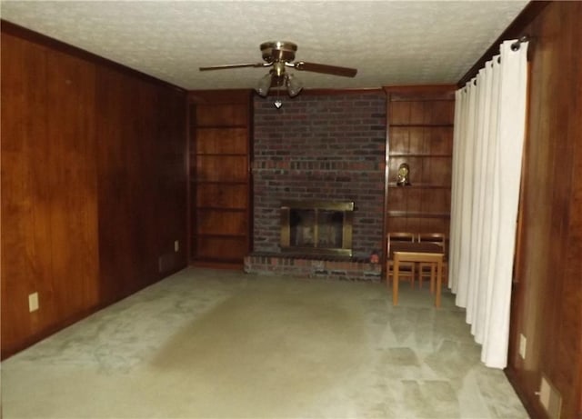 unfurnished living room with a textured ceiling, ceiling fan, a fireplace, and wooden walls