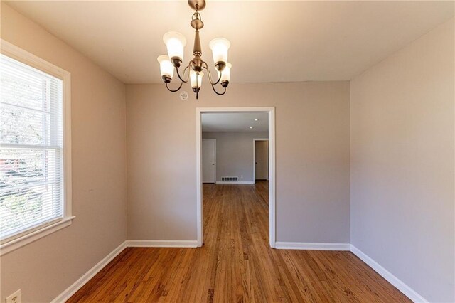 unfurnished dining area with wood-type flooring and an inviting chandelier