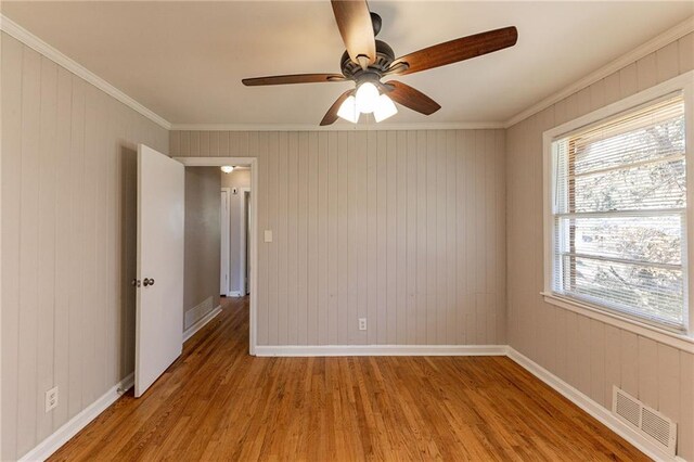 spare room featuring ceiling fan, crown molding, wooden walls, and light hardwood / wood-style flooring