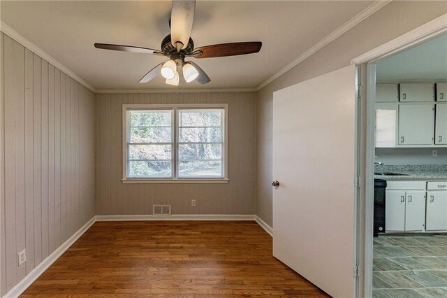 spare room featuring ceiling fan, wooden walls, crown molding, sink, and light hardwood / wood-style floors