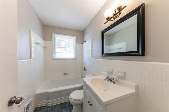 full bathroom featuring tile patterned floors, toilet, vanity, tile walls, and tiled shower / bath