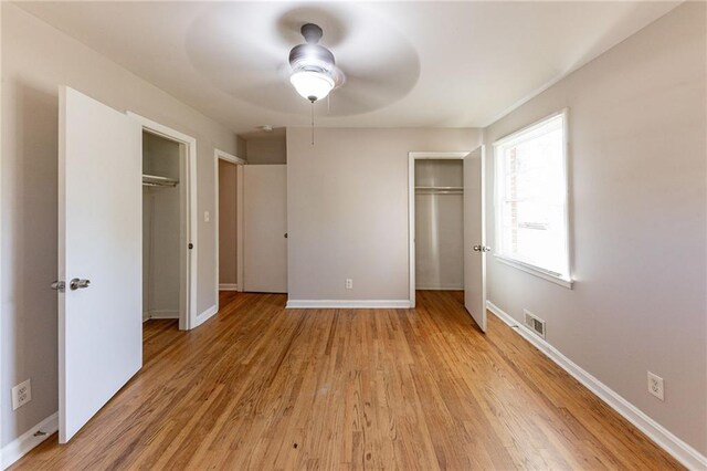 unfurnished bedroom featuring two closets, light hardwood / wood-style floors, and ceiling fan