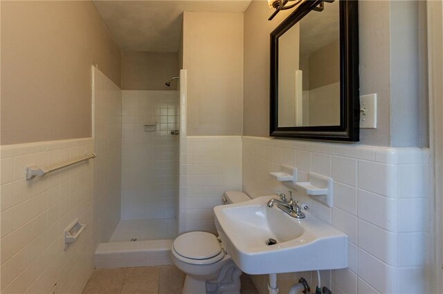 bathroom featuring tiled shower, toilet, tile walls, and sink