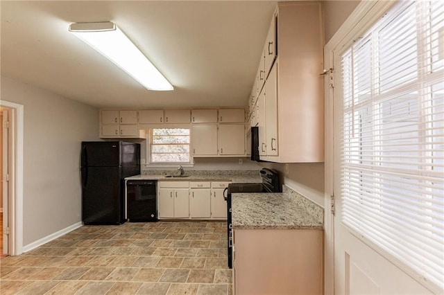 kitchen with cream cabinets, light stone countertops, sink, and black appliances