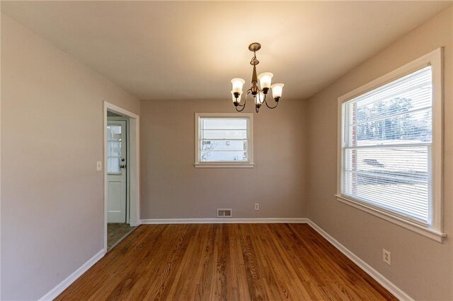 unfurnished room with a notable chandelier and dark hardwood / wood-style flooring