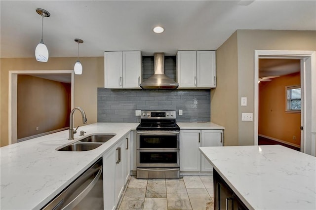 kitchen with appliances with stainless steel finishes, wall chimney exhaust hood, sink, decorative light fixtures, and white cabinets