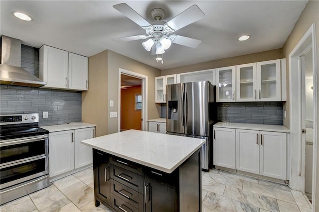 kitchen with decorative backsplash, stainless steel appliances, white cabinetry, and wall chimney range hood