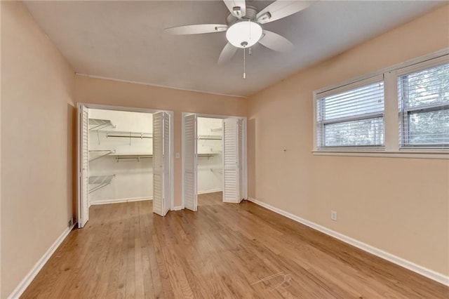 unfurnished bedroom featuring light hardwood / wood-style floors, ceiling fan, and multiple closets