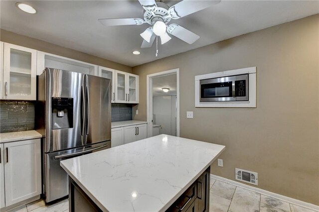 kitchen with backsplash, white cabinets, appliances with stainless steel finishes, a kitchen island, and light stone counters