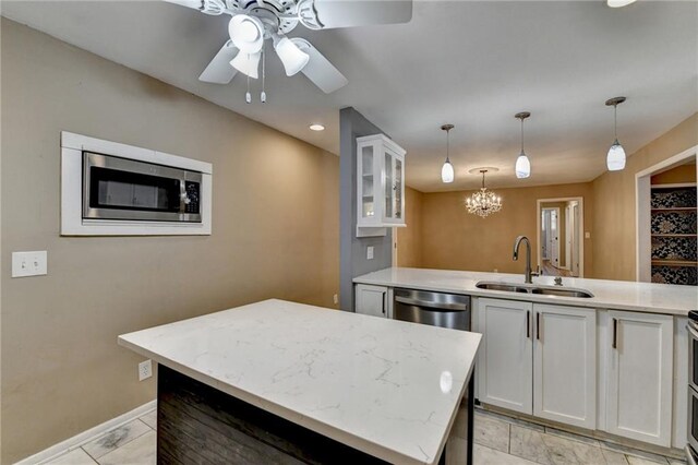 kitchen with ceiling fan with notable chandelier, stainless steel appliances, sink, white cabinetry, and hanging light fixtures