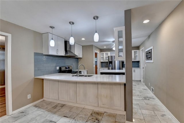 kitchen with kitchen peninsula, stainless steel appliances, sink, wall chimney range hood, and white cabinetry