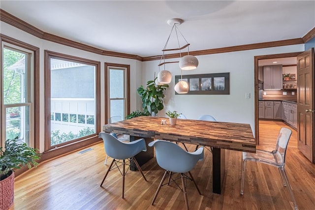 dining room featuring visible vents, crown molding, a healthy amount of sunlight, and light wood-type flooring