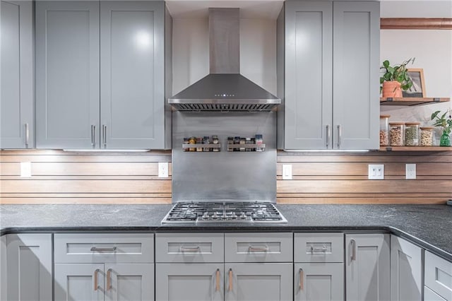kitchen featuring dark stone counters, gray cabinets, stainless steel gas cooktop, and wall chimney exhaust hood