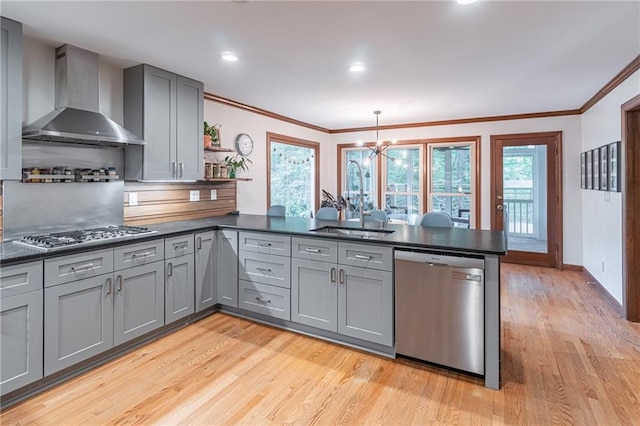 kitchen with a peninsula, dark countertops, wall chimney range hood, gray cabinets, and appliances with stainless steel finishes