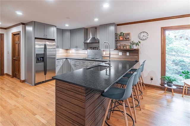 kitchen with wall chimney range hood, crown molding, a breakfast bar area, stainless steel appliances, and gray cabinetry