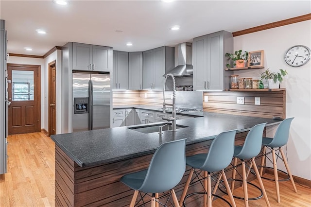 kitchen featuring crown molding, dark countertops, stainless steel fridge, wall chimney exhaust hood, and gray cabinetry