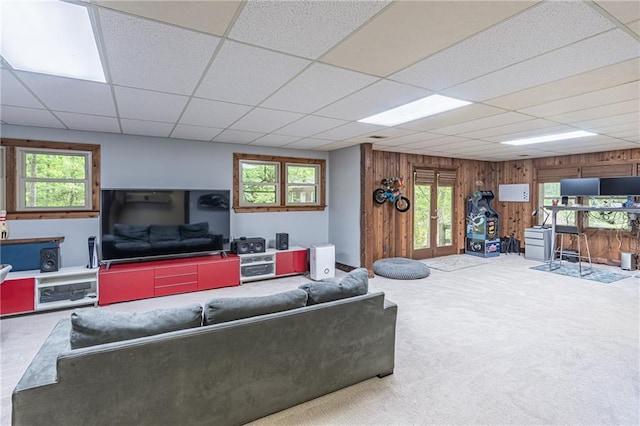 carpeted living area featuring a paneled ceiling, wooden walls, and a wealth of natural light
