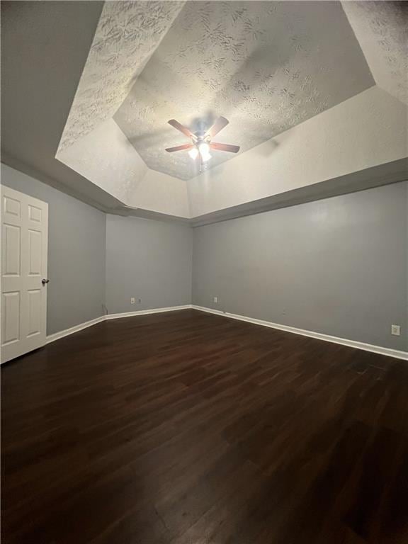 spare room featuring a ceiling fan, dark wood-style flooring, baseboards, a textured ceiling, and lofted ceiling
